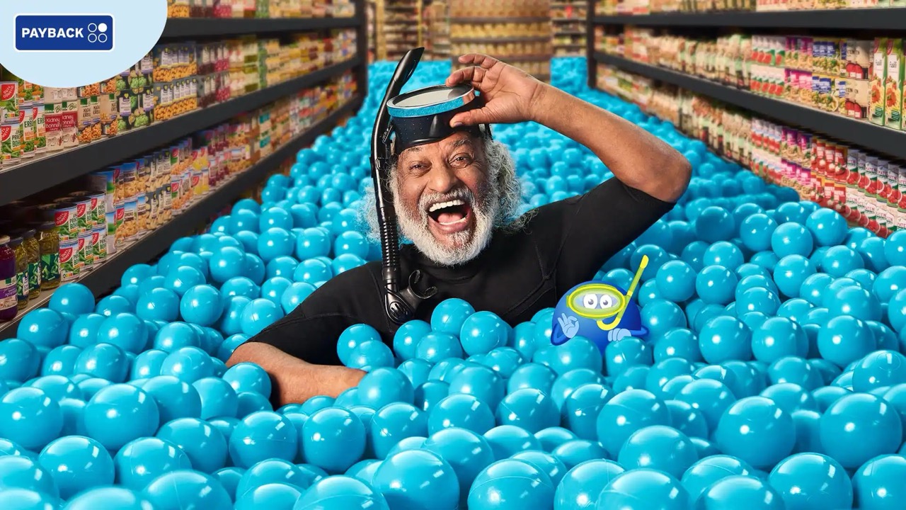 Älterer Mann mit grauem Vollbart ist in einem Supermarktgang bis zu den Schultern in blauen Bällen versunken. Er trägt eine Taucherbrille mit Schnorchel.