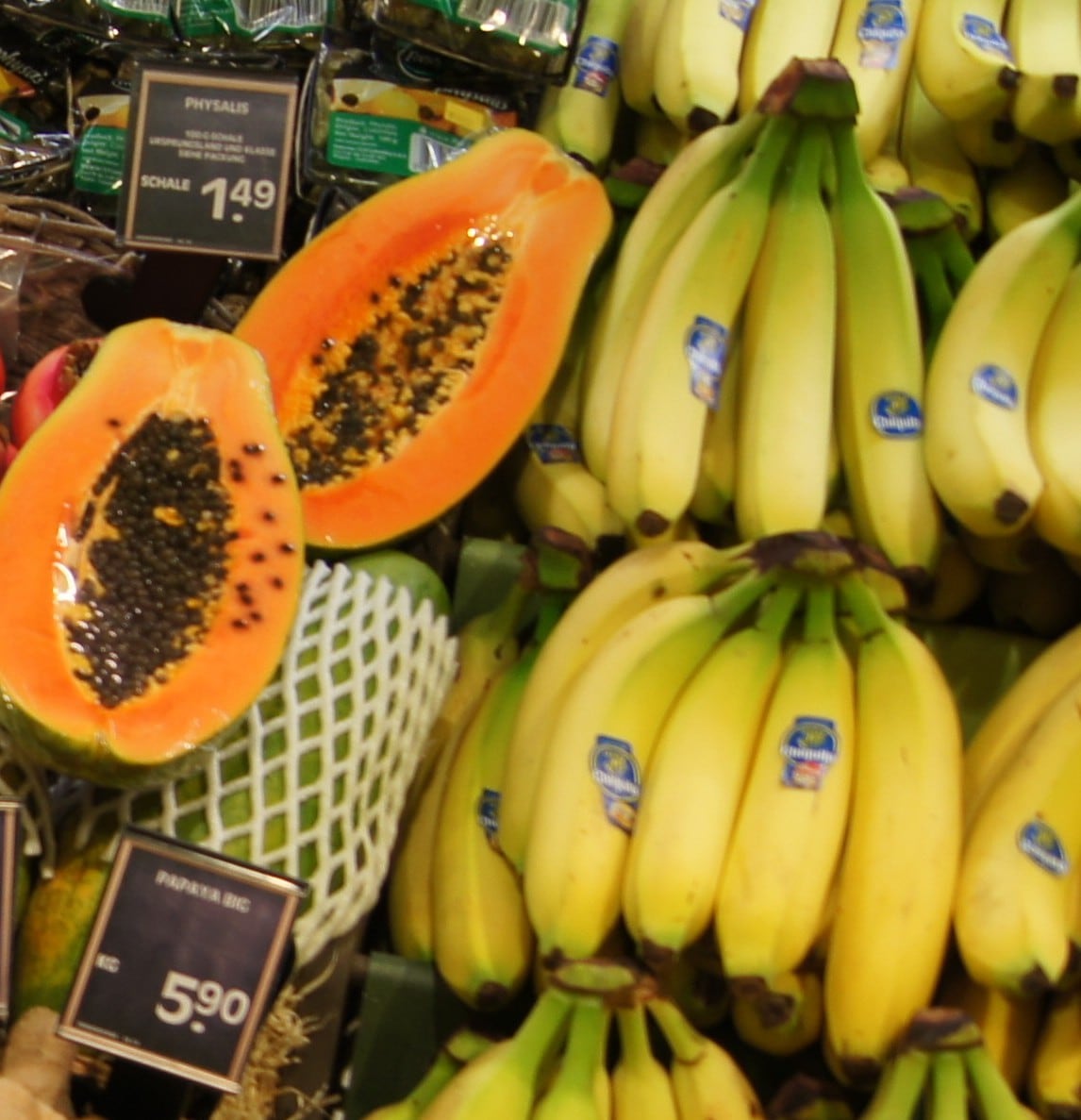Nahaufnahme zweier aufgeschnittener Papaya-Hälften sowie Bananen.