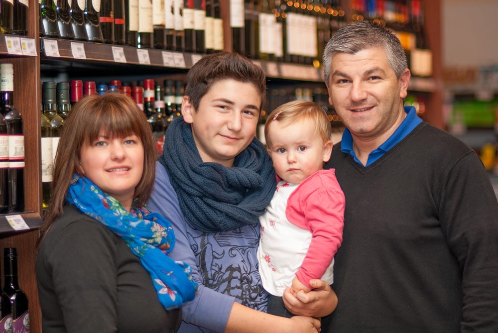 Inhaber Sedat Karavil steht mit seiner Familie vor einem Weinregal.