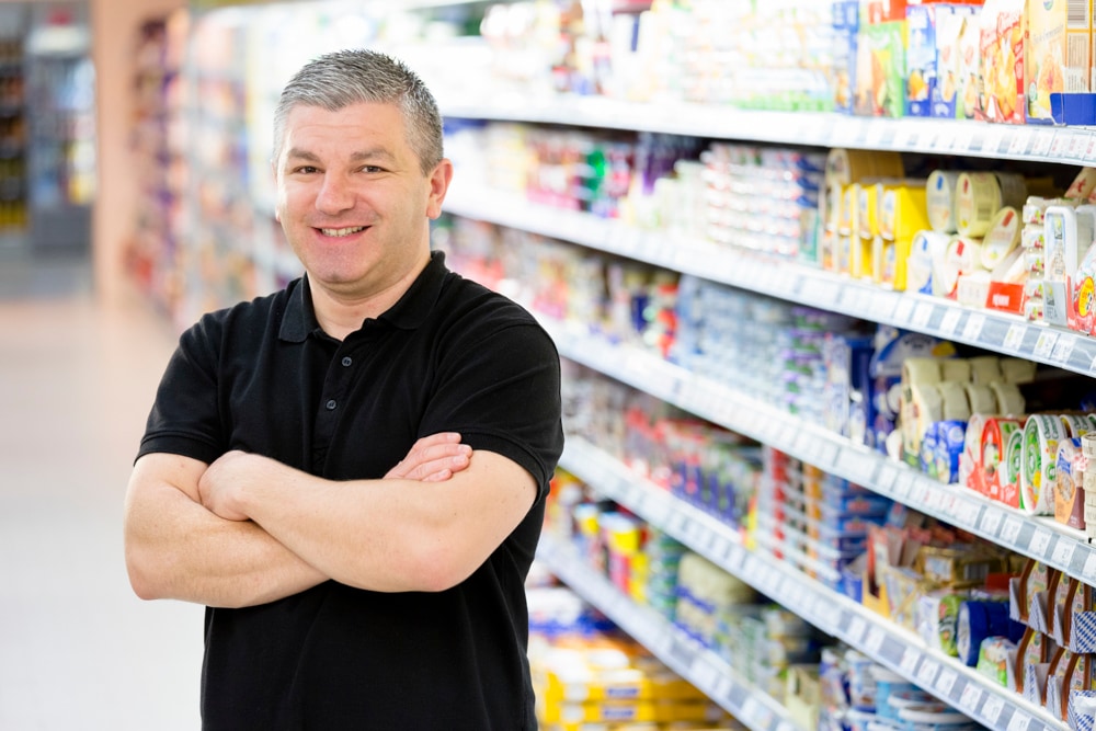 Inhaber Sedat Karavil steht mit verschränkten Armen vor einem Regal.