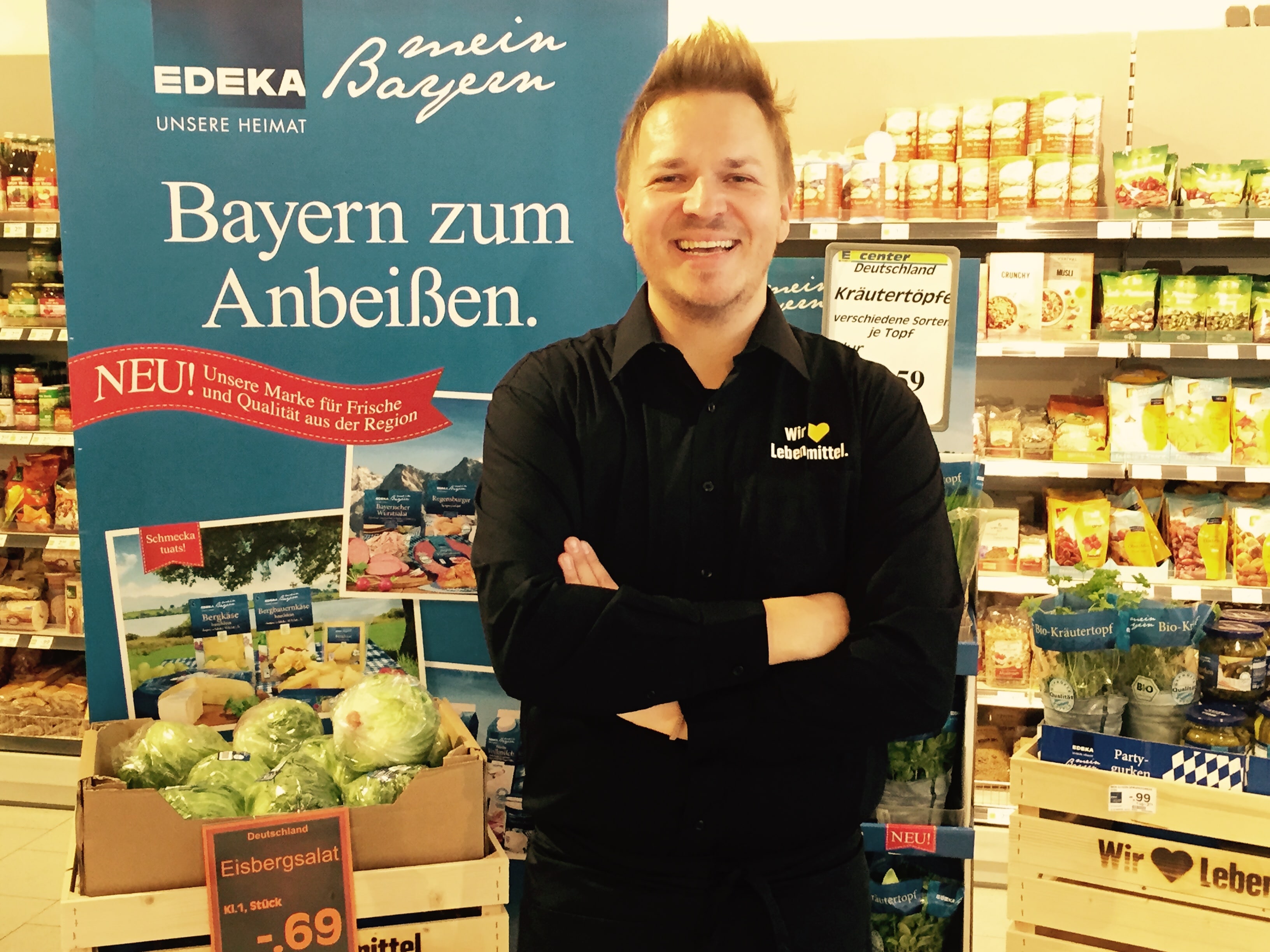 Inhaber Florian van Dungen steht mit verschränkten Armen vor einem großen Auftsteller, auf dem steht: Bayern zum Anbeißen.