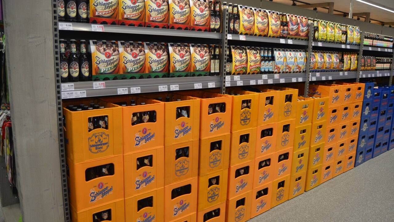 Gestapelte Bierkisten unterhalb eines Regals mit einzelnen Bierflaschen.