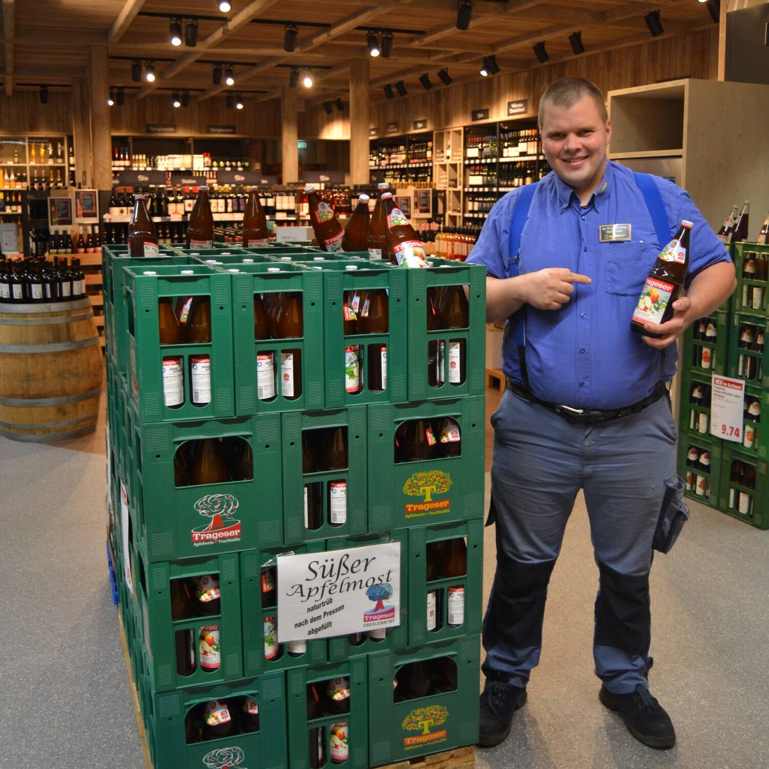 Ein lächelnder Mitarbeiter eines Getränkemarktes zeigt auf eine Flasche Saft die er in der Hand hält.