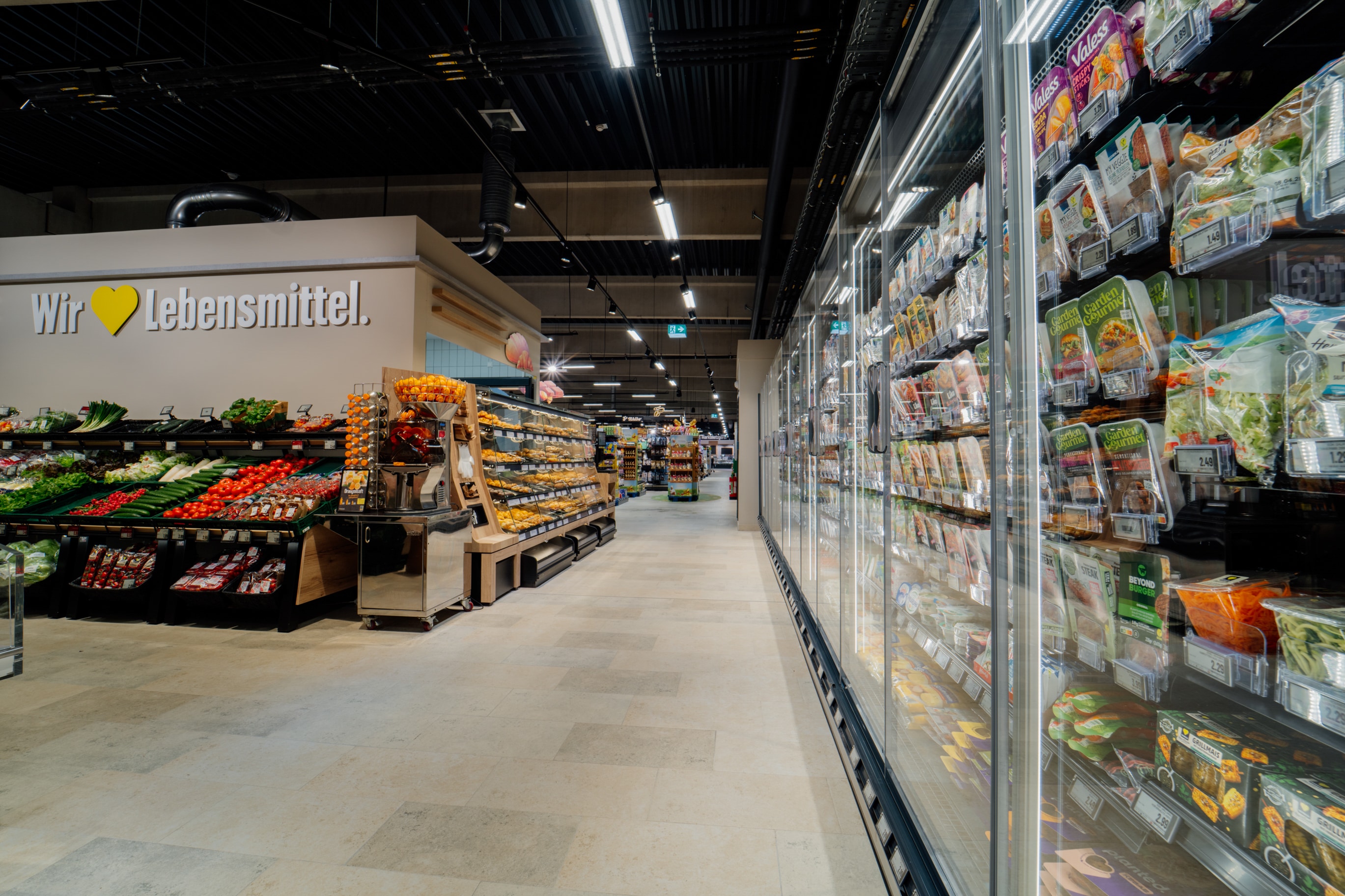 Innenansicht eines modernen EDEKA-Marktes mit Obst- und Gemüseabteilung sowie Kühlregalen.