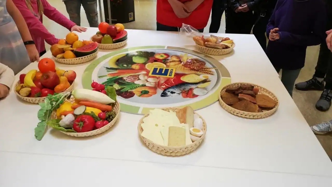Gedeckter Tisch mit Gemüsesorten auf einem Teller, Obst auf drei weiteren sowie Brotsorten.