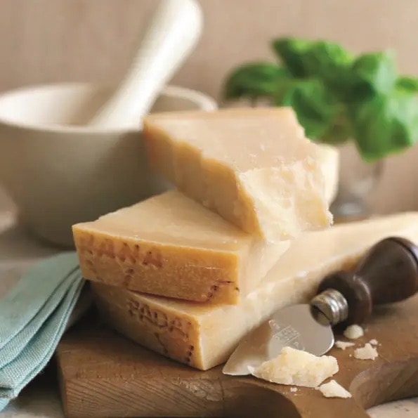 Drei große Stücke Parmesan Hartkäse übereinander auf einem Holzbrett gestapelt.