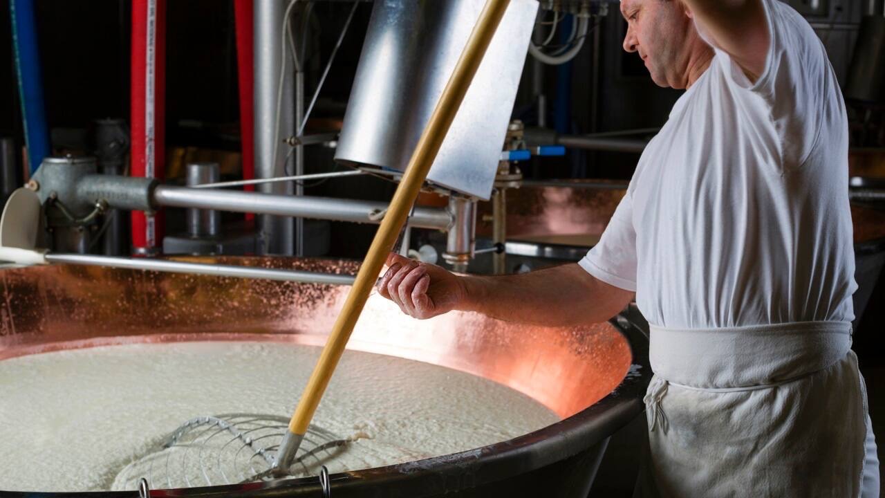 Ein Mann mit weißer Schürze rührt in einem kupferfarbenen Metallbehälter mit weißer Masse.