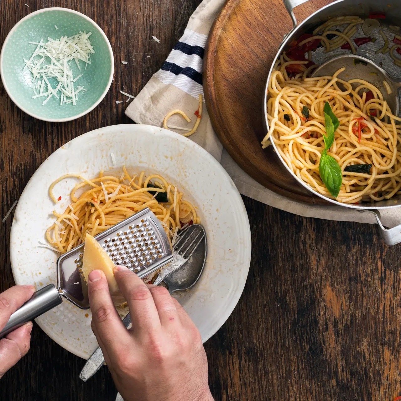 Eine Person reibt Käse über einen Teller mit Spaghetti.