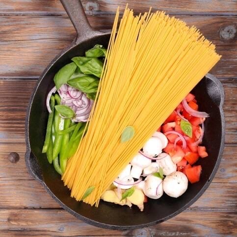 Eine tiefe Pfanne gefüllt mit Zwiebeln, Bohnen, Basilikum, Pilzen, Tomaten und Spaghetti.