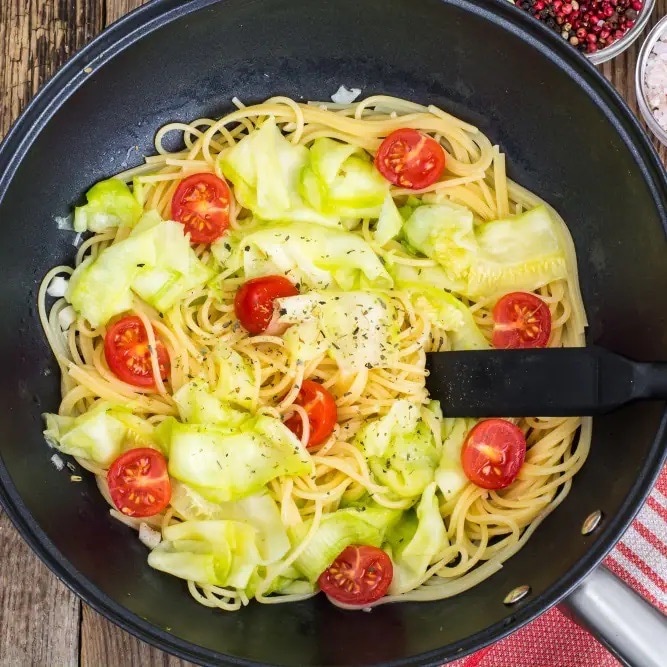 Spaghetti mit Lauch und Kirschtomaten in einem schwarzen Topf.