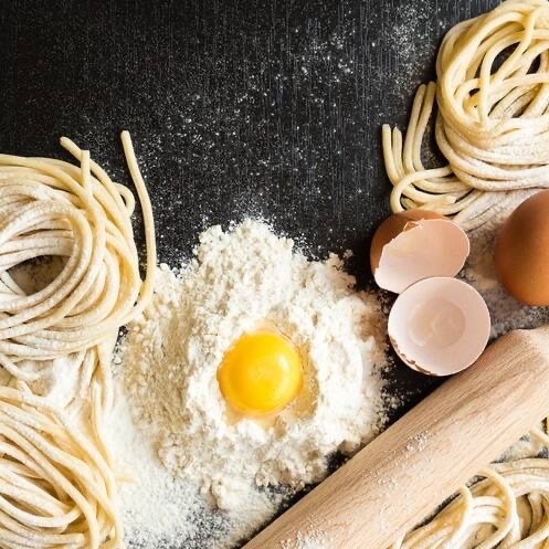 Rohe Spaghetti, Nudelholz und ein Eigelb in einer Mehlmulde.
