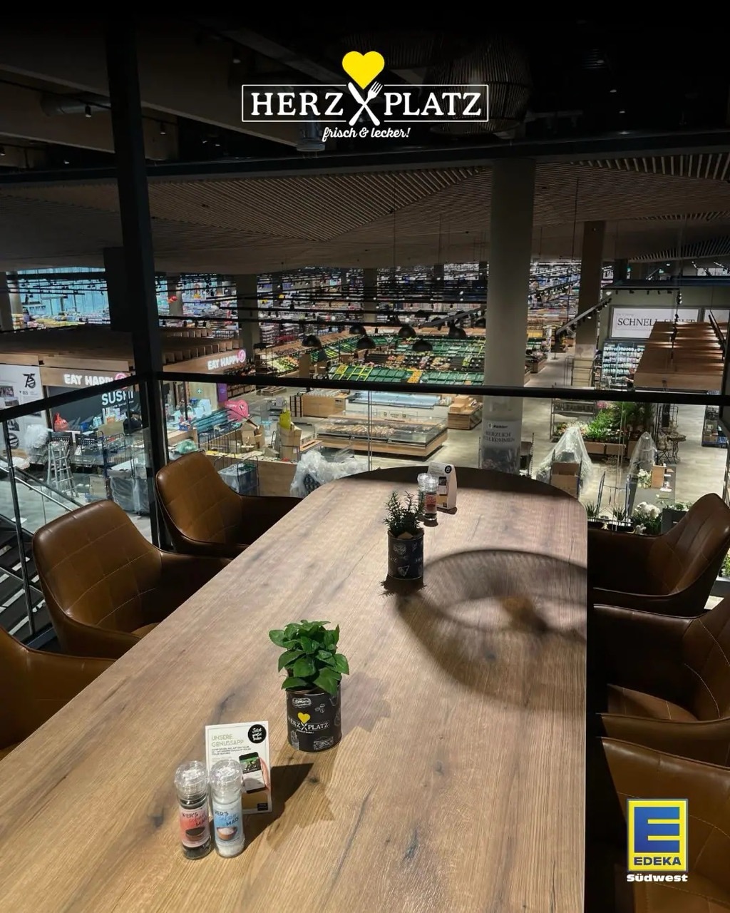 Langer Tisch mit sechs Sesseln im Restaurant Herzplatz. Blick herunter rauf den EDEKA-Markt.