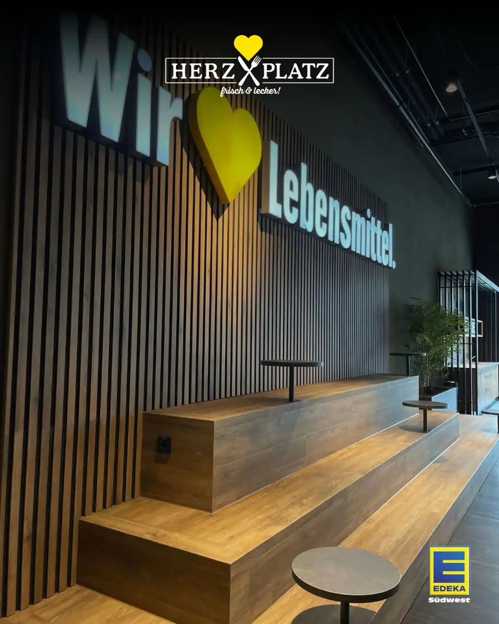 Dreistufige Holzempore mit Sitzmöglichkeiten. Dahinter an der Wand Holzpanele und der Slogan Wir lieben Lebensmittel.