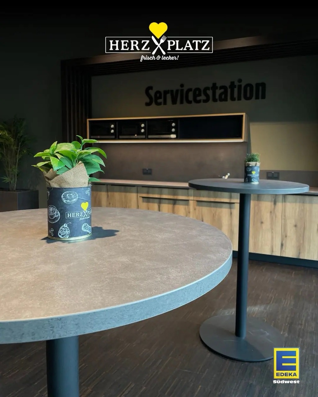 Zwei runde Stehtische mit Kräutertöpfen vor der Servicestation.