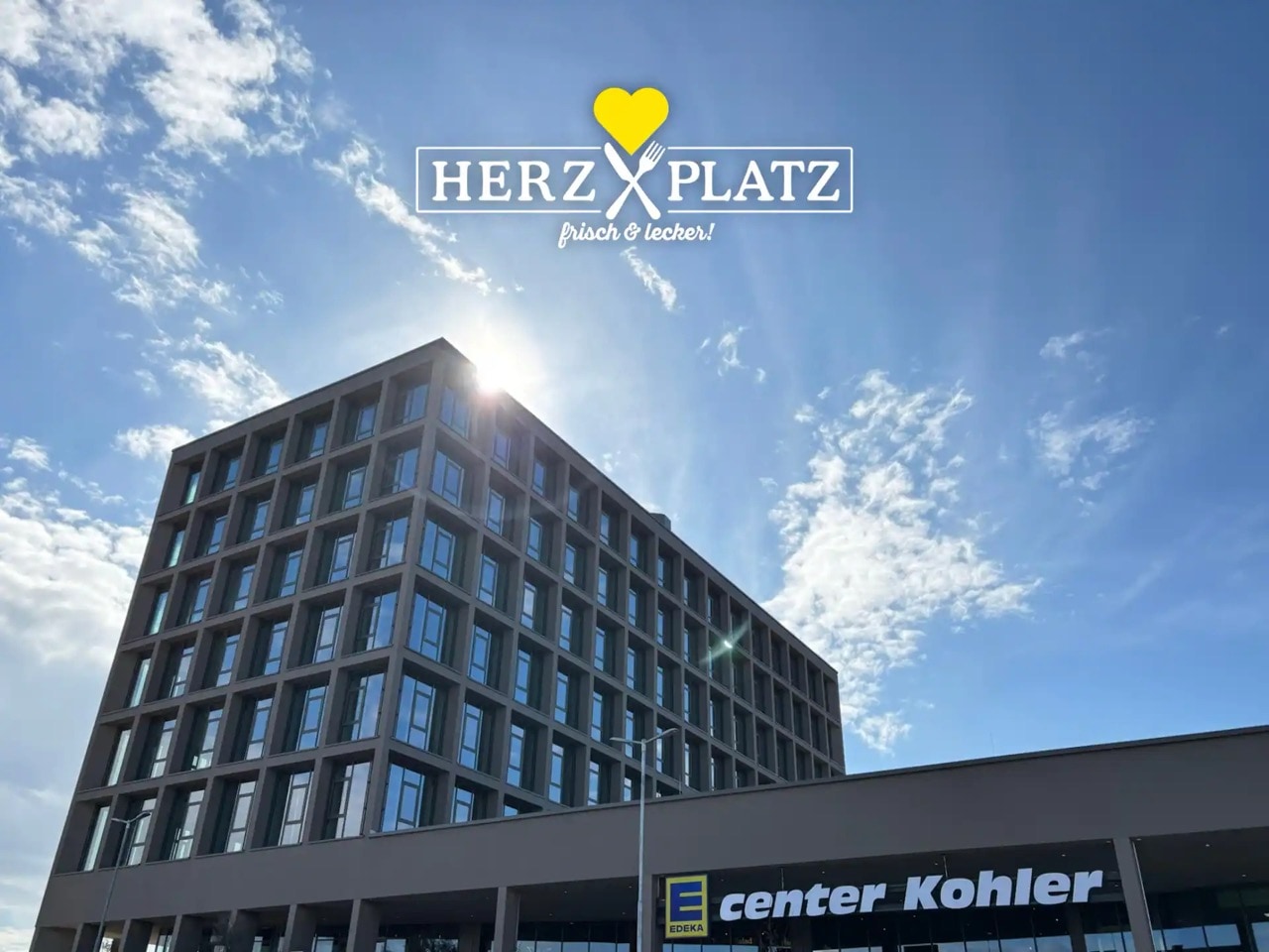 Sechsstöckiger Bau über dem EDEKA center Kohler unter blauem Himmel. Logo Restaurant Herzplatz. Frisch und lecker.