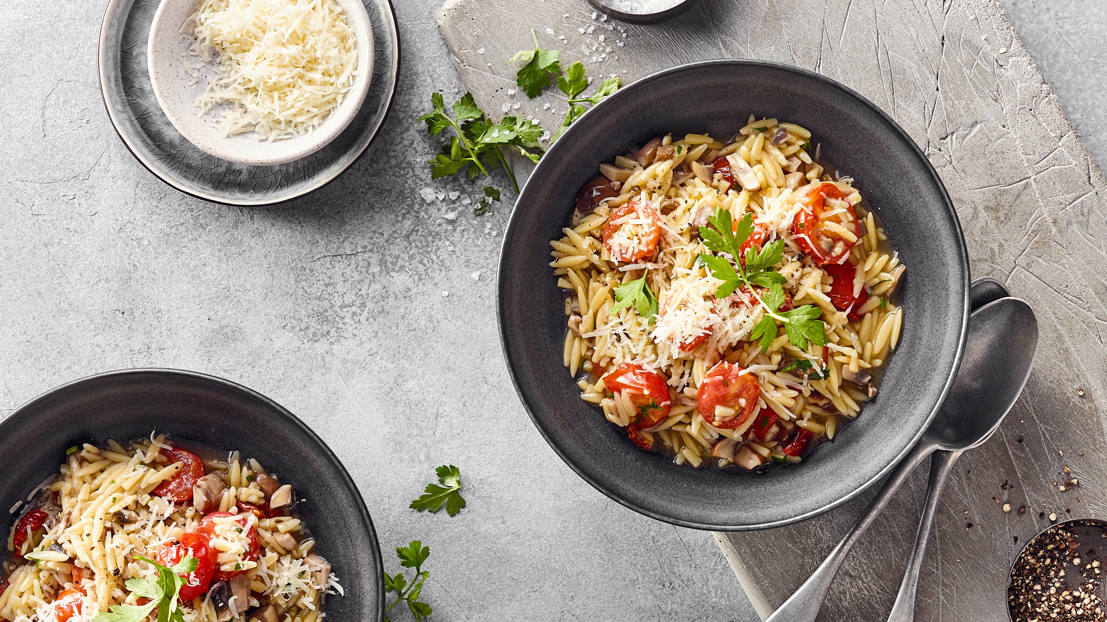 Eine Schale mit Orzonudeln, Kirschtomaten und Champignons, getoppt mit geriebenem Käse und frischer Petersilie
