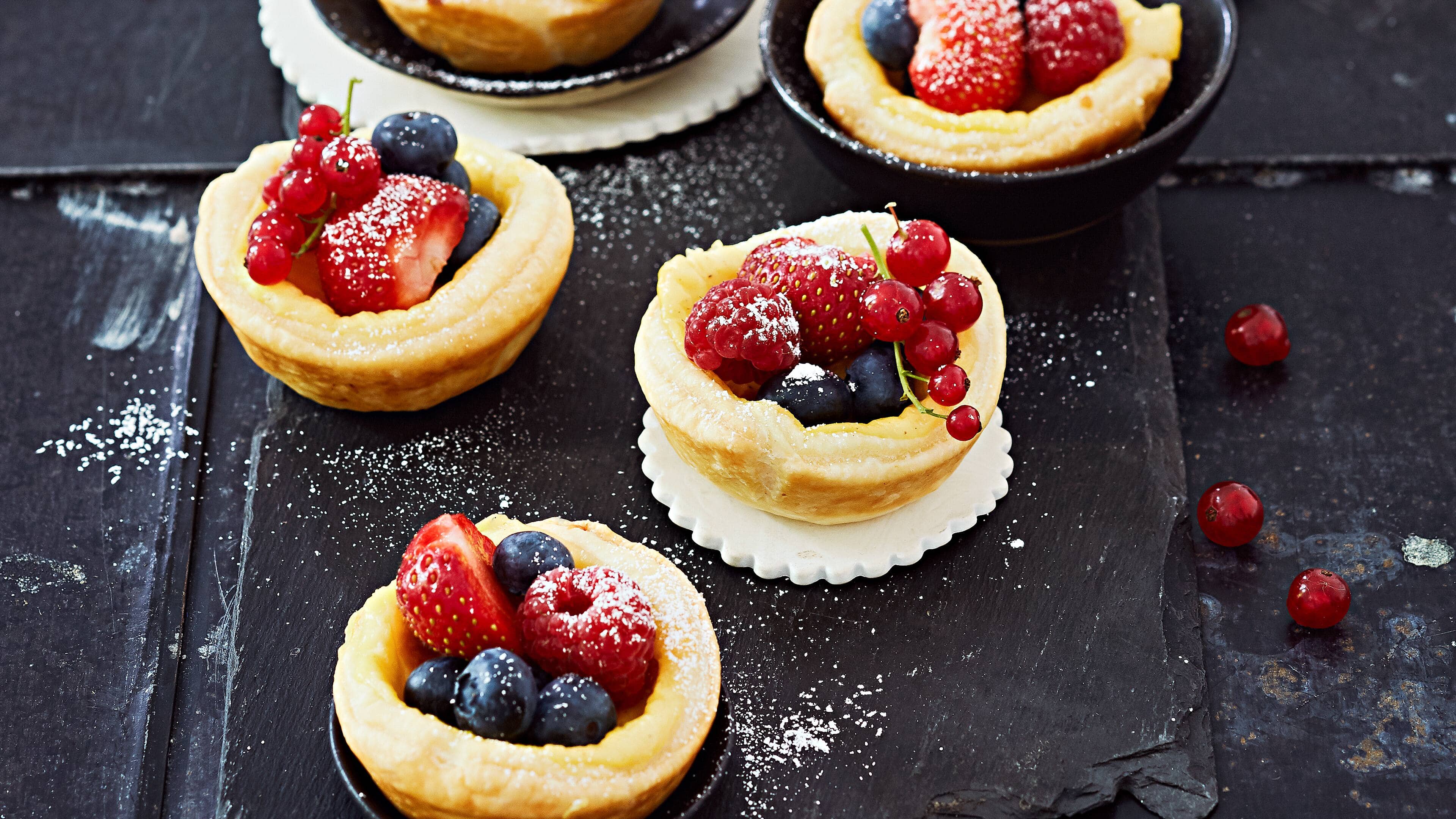 Vanilletörtchen mit Beeren Die essbaren Obstkörbchen sind ideal, wenn es mal schnell gehen muss und trotzdem was hermachen soll. Der Blätterteig stammt aus dem Kühlregal und wird mit Vanillepudding ergänzt. Genießen Sie die Vanilletörtchen mit frischen Beeren.