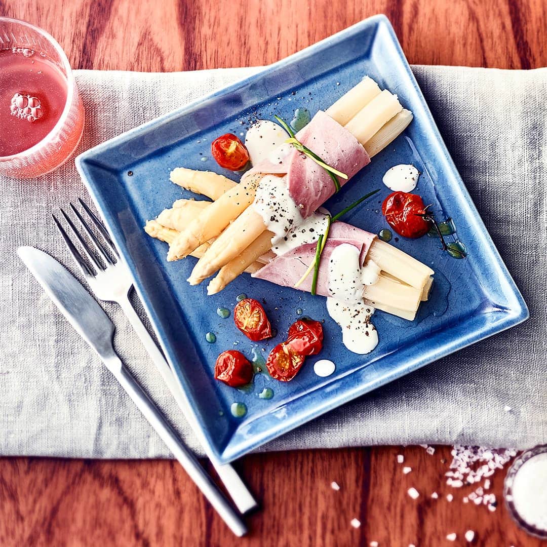 Diese leckere Zwischenmahlzeit schmeckt nach Sommer: Probieren Sie unser Rezept für Röllchen aus weißem Spargel mit gekochtem Schinken und gegrillten Cocktailtomaten an leichter Joghurt-Soße einmal aus – fertig in 50 Minuten!