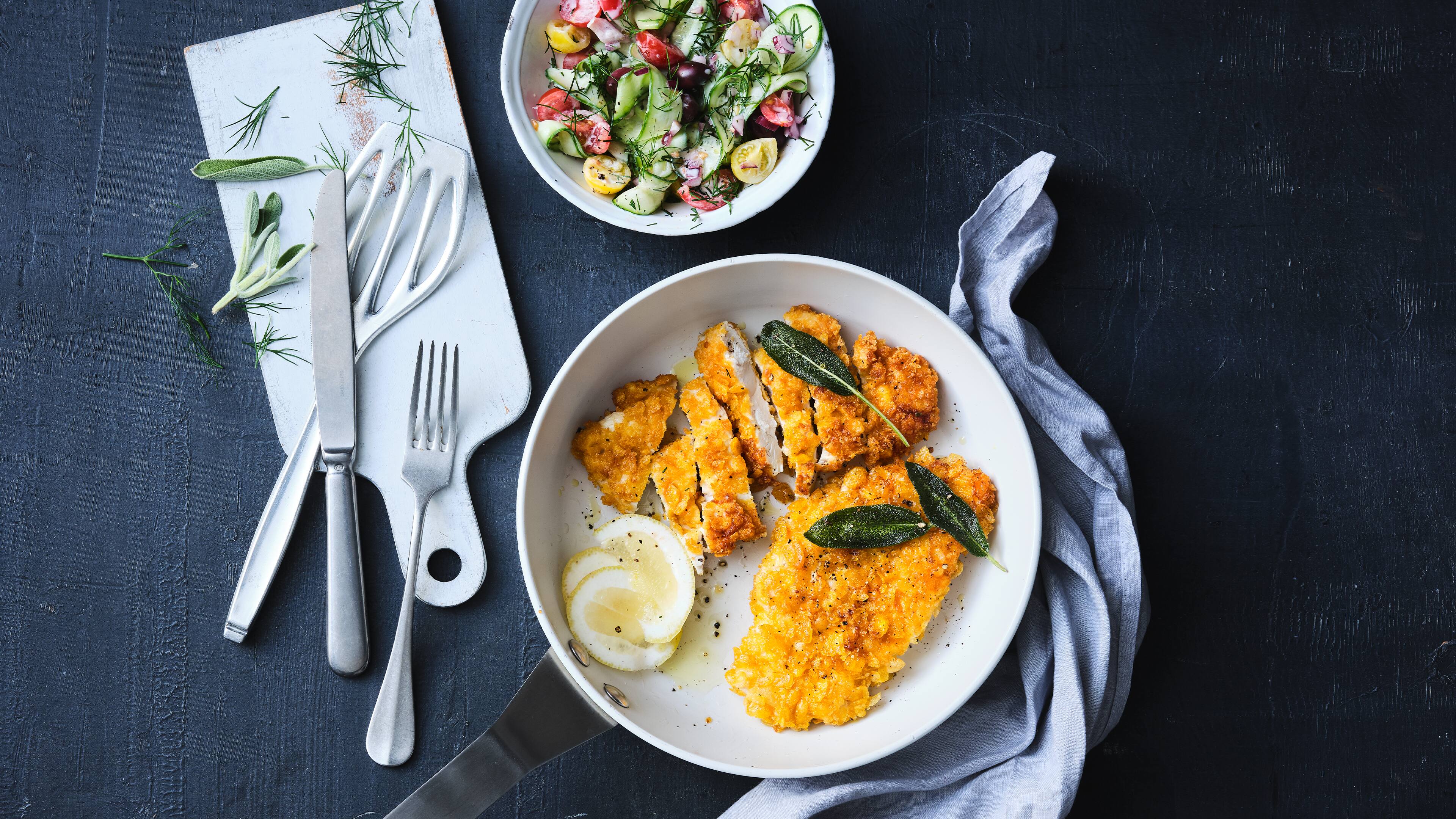 Knusper-Schnitzel mit Gurkensalat Die Cornflakes sorgen für eine richtig leckere und krosse Panade in unserem schnellen Rezept für Knusper-Schnitzel mit selbstgemachtem Gurkensalat.