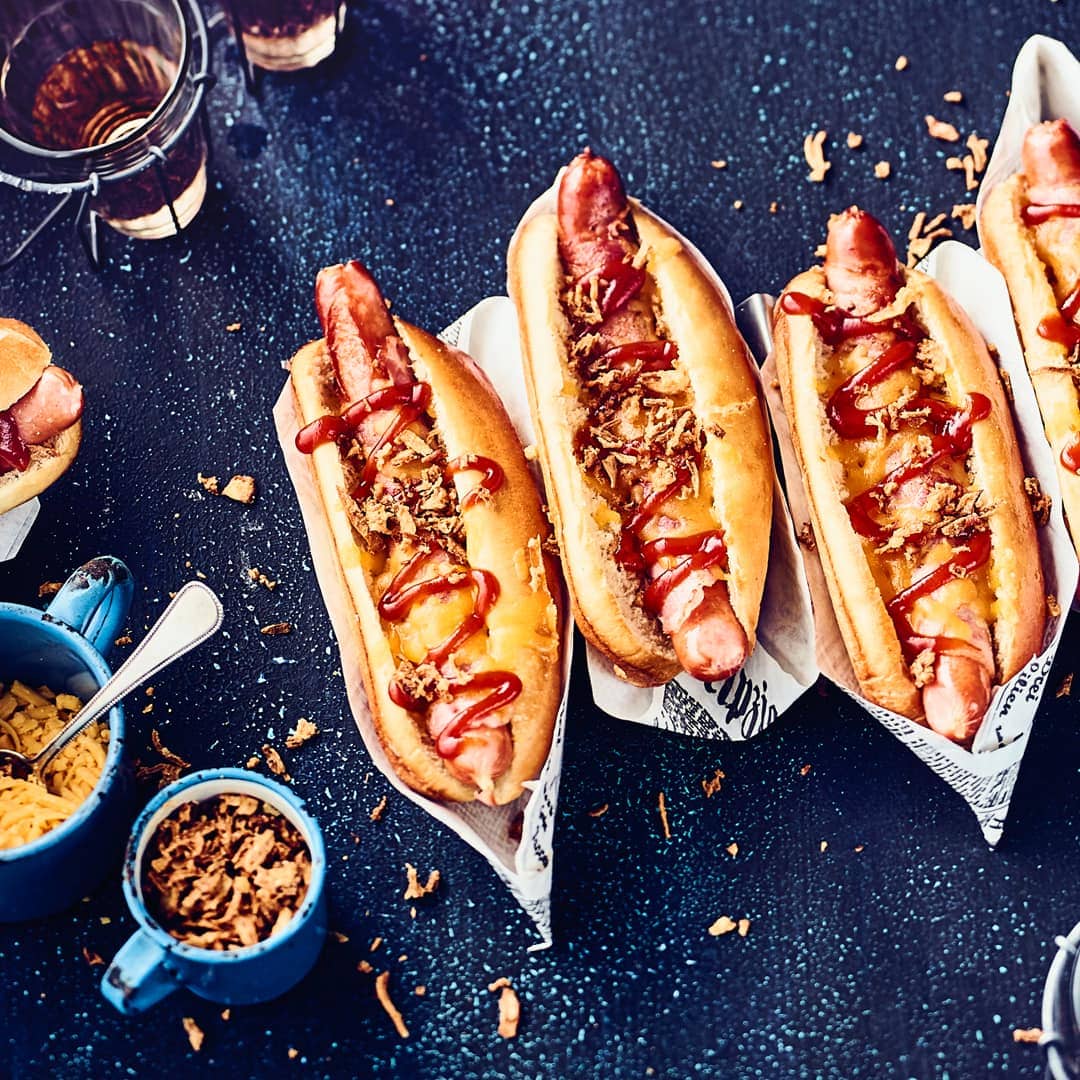 Leckere Brioche Hot Dog Buns gefüllt mit mit Bacon umwickelten Würstchen und garniert mit selbstgemachter BBQ-Soße und Röstzwiebeln - ein wahrer Genuss!