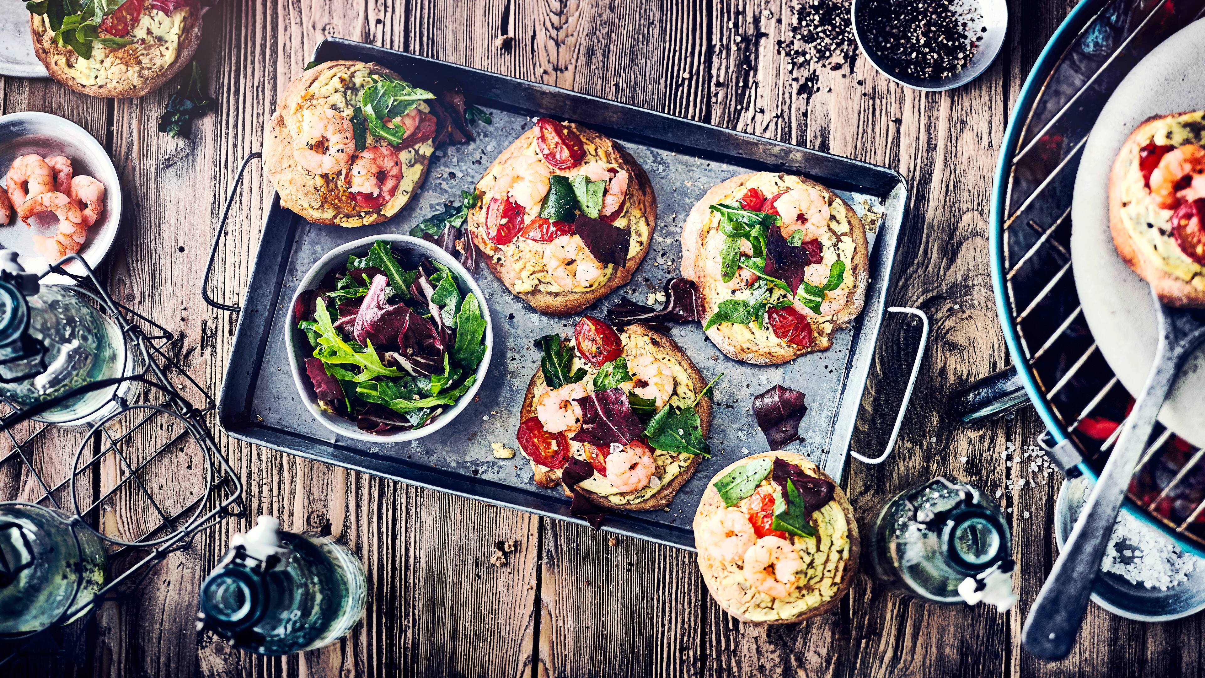 Mini-Salatpizza vom Grill Warum Pizza immer nur aus dem Ofen? Im Sommer schmeißen wir doch viel lieber den Grill an: Genießen Sie unsere kleinen Mini-Salatpizzen mit Garnelen, Tomaten und Rucola!