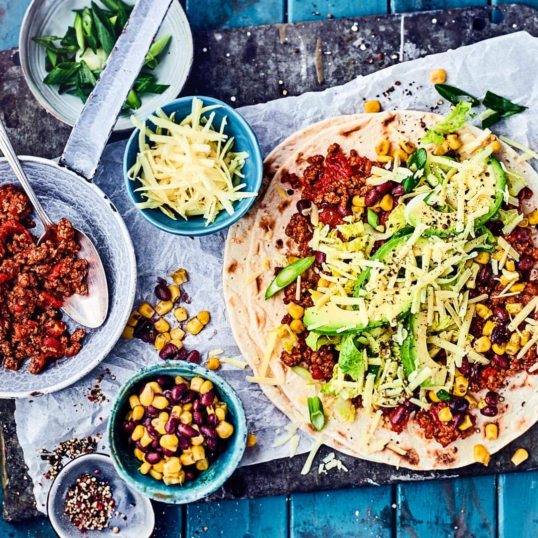 Feuriger Burrito mit Hackfleisch-Tomatensauce, würzigem Cheddar, Salat, Mais und Avocado. Mit Sour Cream genießen.