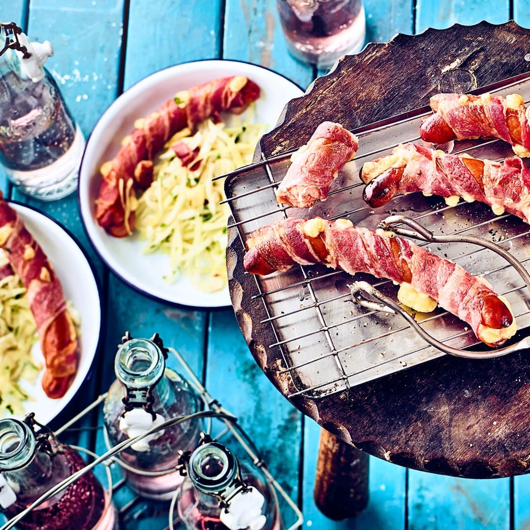 Wiener Würstchen aufgeschnitten, mit Käse gefüllt und mit Frühstücksspeck umwickelt serviert mit Schweizer Speck-Kraut-Salat aus der Schweiz.