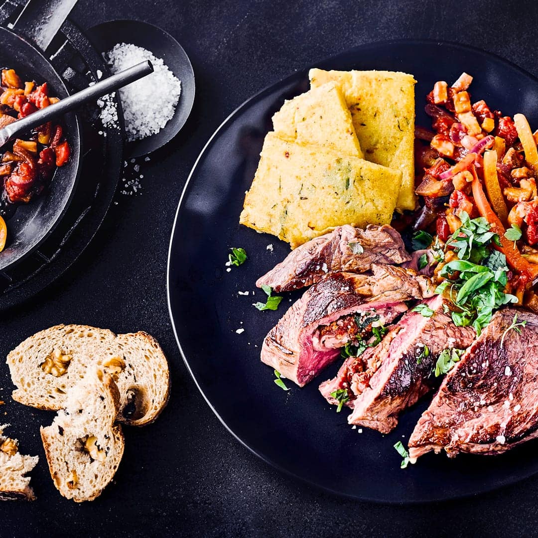 xxxMediterrane Köstlichkeit: Probieren Sie unsere mit Schinken, Oliven und getrockneten Tomaten gefüllten Rindersteaks an geschmortem Gemüse und Polenta!