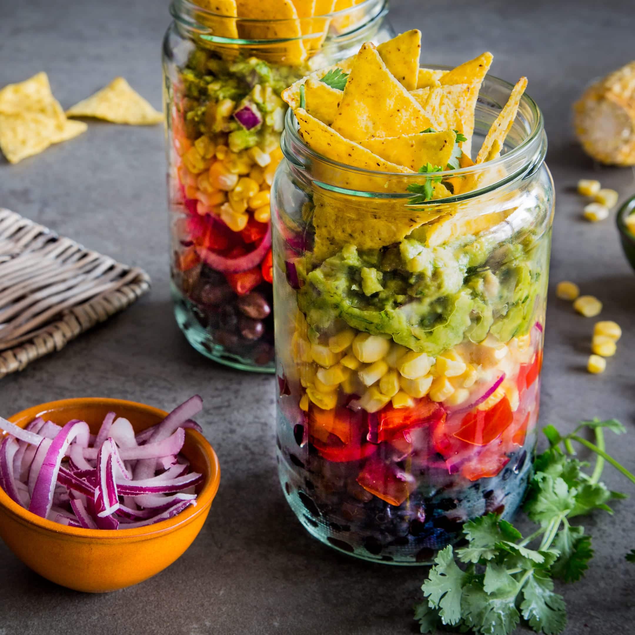 Mexikanisch einmal anders: Selbstgemachter Nacho-Salat im Glas aus Bohnen, Mais, Salat, Salsa, Guacamole und mit Tortilla-Chips-Topping.