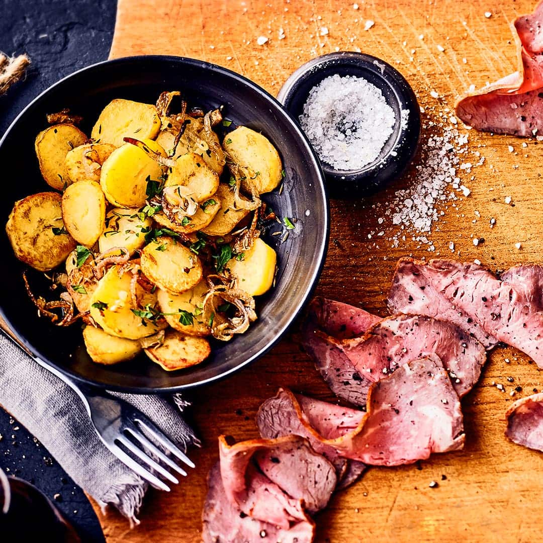 Ein klassischer Mittagstisch: Gebratenes Roastbeef in dünne Scheiben geschnitten, mit Bratkartoffeln, einer würzigen Zwiebel-Pilz-Pfanne und selbstgemachter Remoulade serviert.
