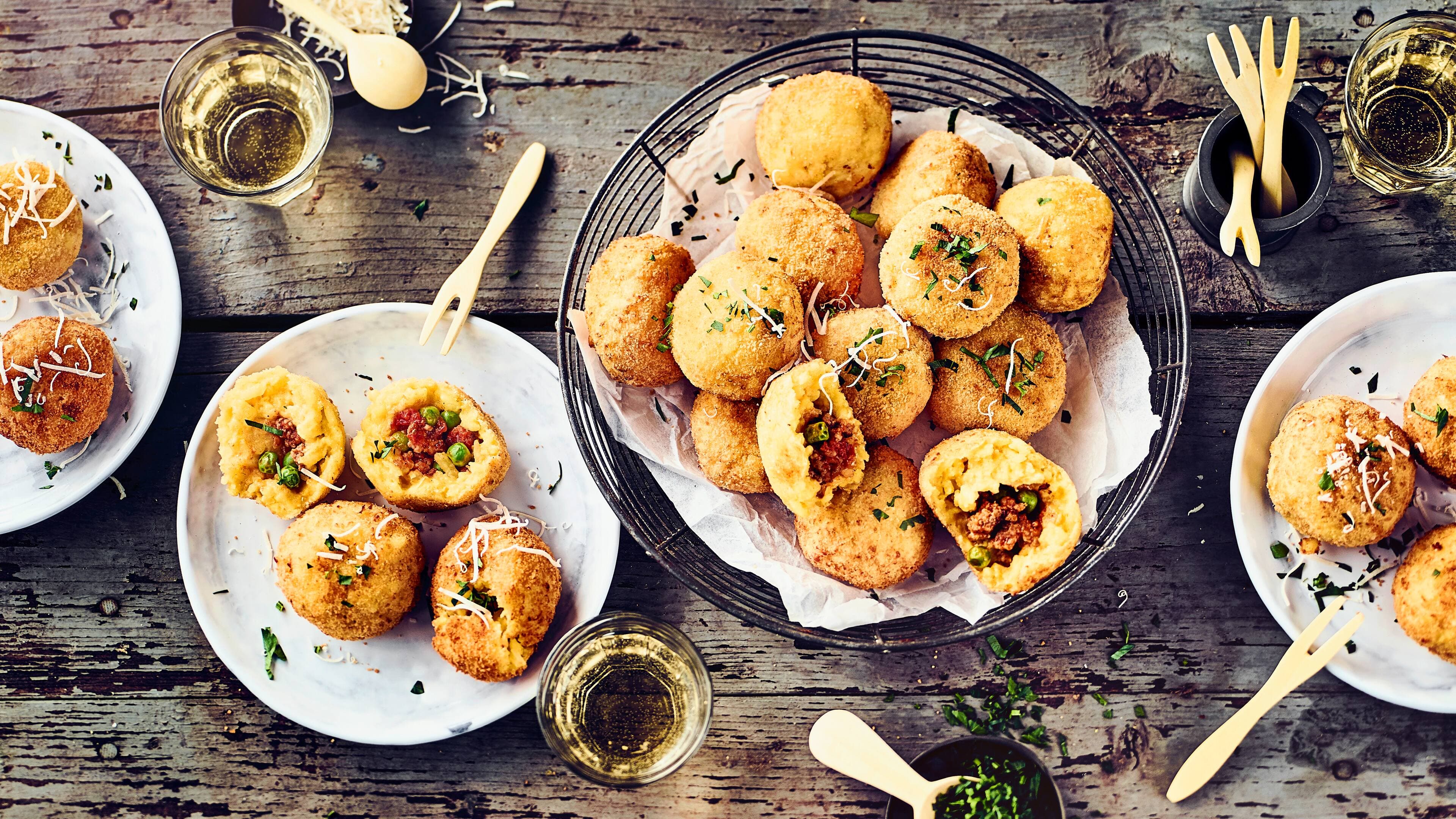 Arancini Bällchen Arancini Bällchen sind köstliche kleine frittierte Reis-Bällchen, gefüllt mit Hackfleisch, Speck und Erbsen.
