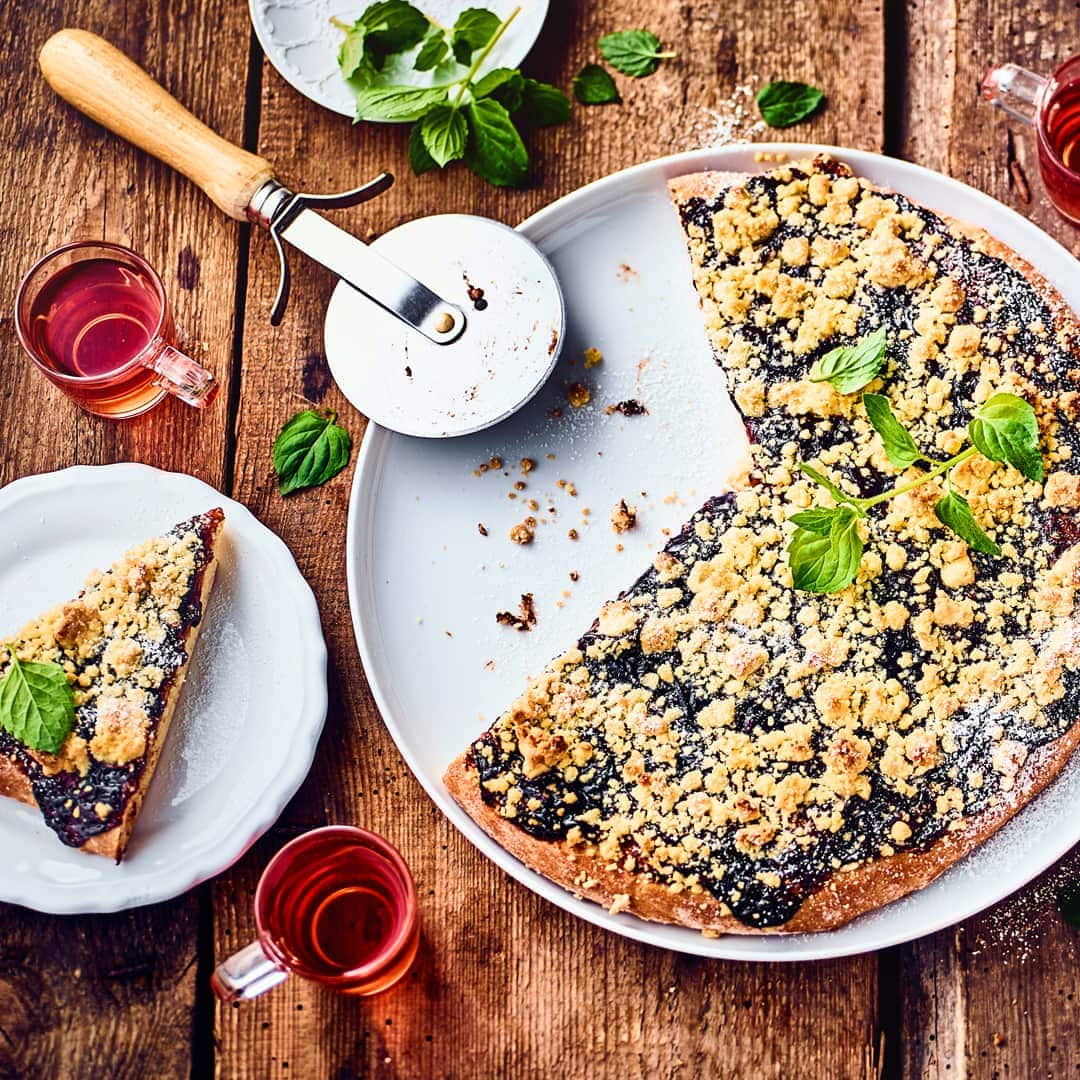 Unser Rezept für süße Pizza interpretiert den Klassiker der italienischen Küche auf unerwartete Weise und kombiniert ihn mit saftigen Pflaumen und zarten Streuseln.