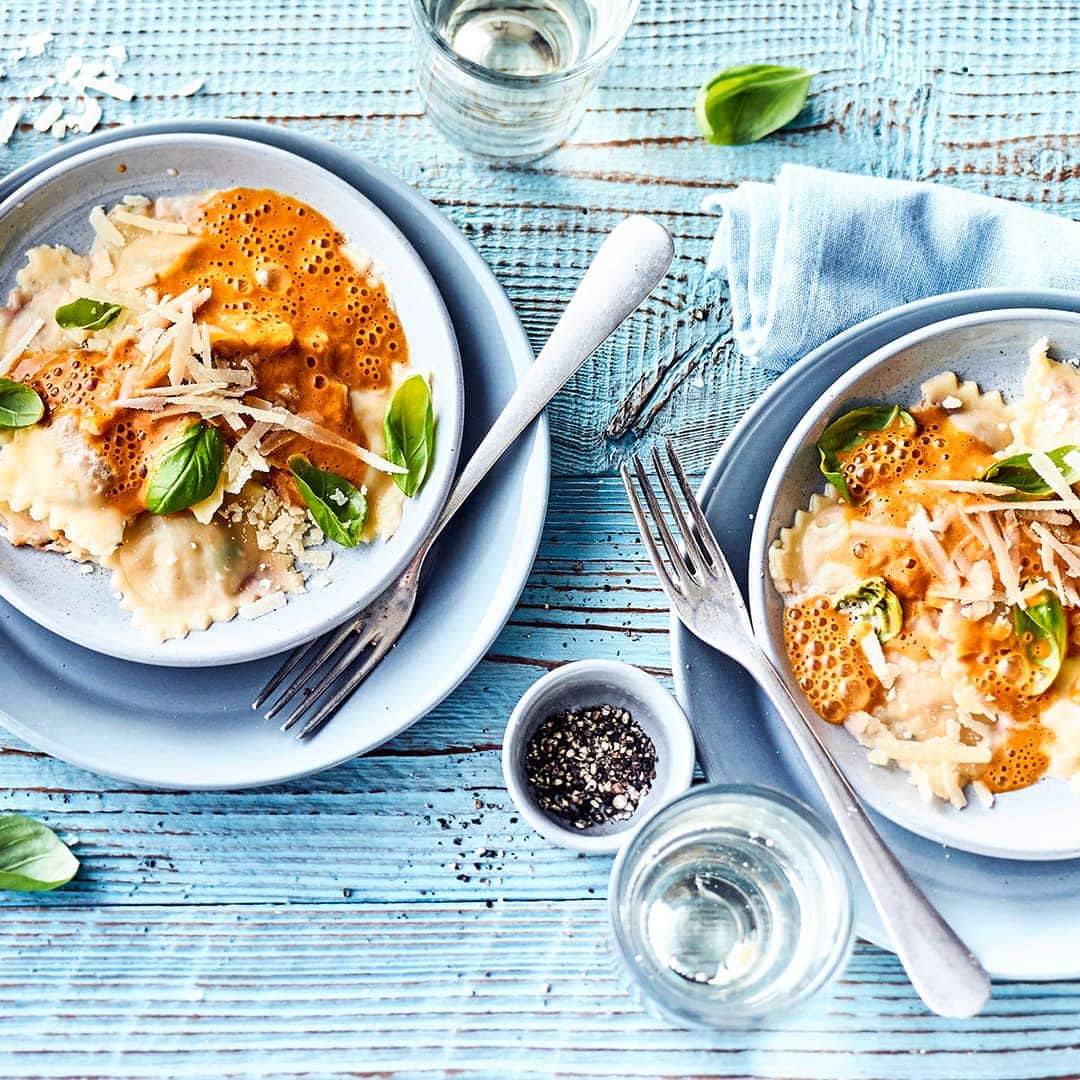 Selbstgemachte Ravioli gefüllt mit einer Mischung aus Parmesan, Oliven und Tomaten, serviert auf einem feinen Paprikaschaum mit Sahne.