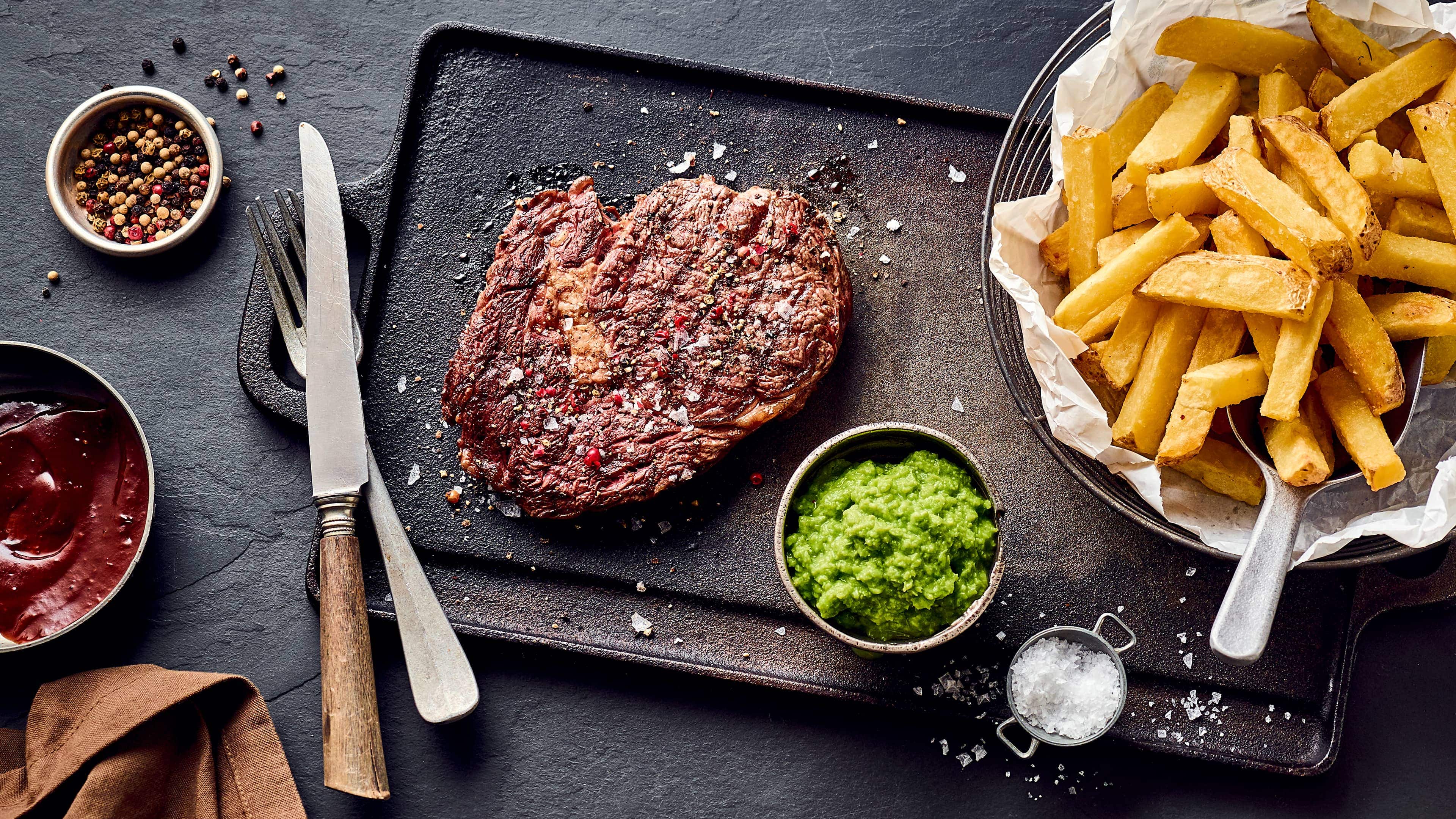 Rib-Eye-Steak mit Pommes Saftiges Rib Eye Steak mit selbst gemachten Pommes frites und exotischem Wasabi-Stampf. Kombinieren Sie Rindfleisch raffiniert mit asiatischer Schärfe.