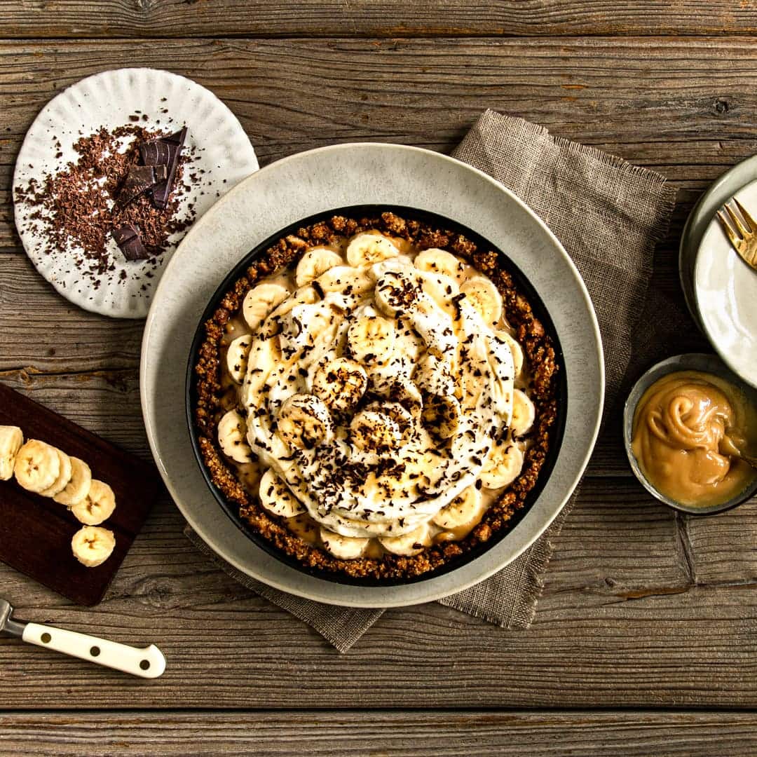 Selbstgemachter Butterkeks-Boden, aus Kondensmilch entstandenes Toffee, Bananenscheiben und eine Sahne-Crème-fraîche-Creme werden nur noch durch und mit Ahornsirup und Schokoladenraspeln getoppt.
