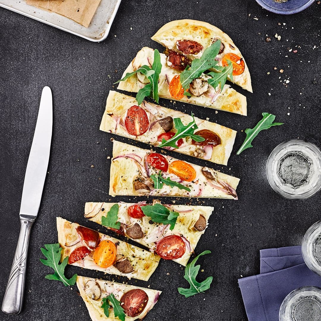 Flammkuchen einmal anders: Als vegetarische Variante präsentieren wir einen Flammkuchen mit Champignons, Zwiebeln, Tomaten und Ziegenfrischkäse.