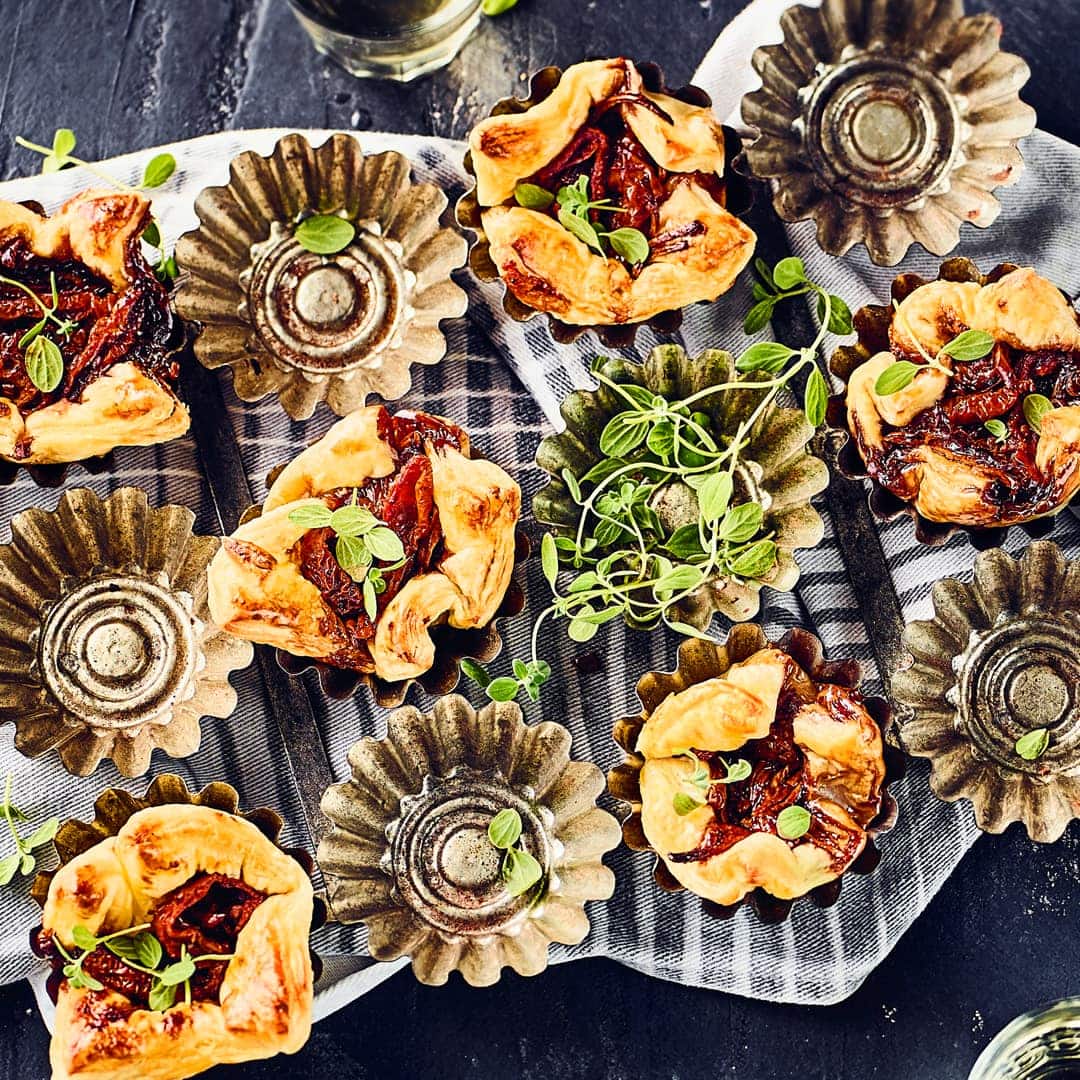 Garantiert der Hingucker auf jeder Party- Probieren Sie unser Rezept für Blätterteigtörtchen mit Tomaten und Zwiebeln in Muffinförmchen gebacken.
