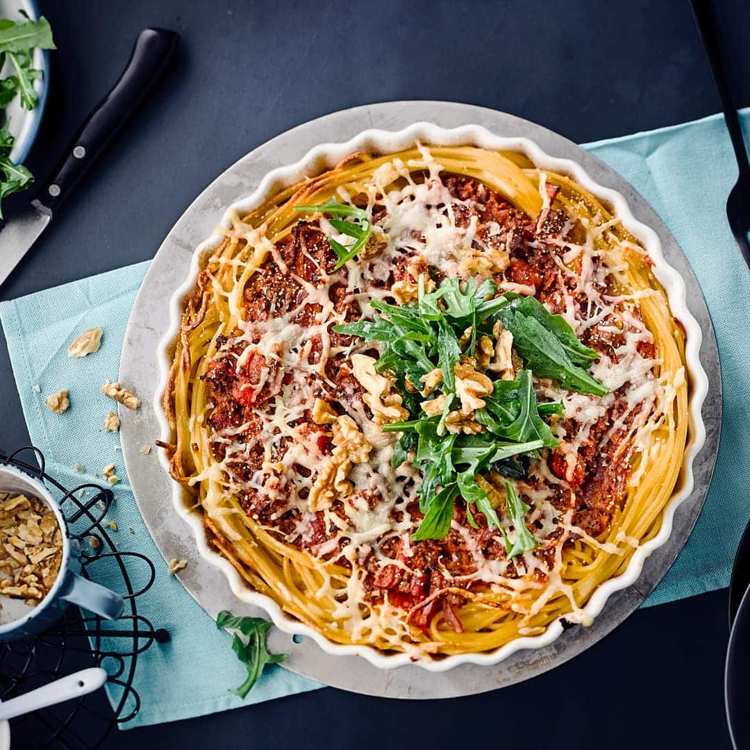 Pasta einmal anders: Verwöhnen Sie Ihre Familie mit unserer Spaghetti-Tarte – gefüllt mit Rinderhack, Mozzarella, Sahne und Karotten, garniert mit frischem Rucola und gehackten Walnüssen!