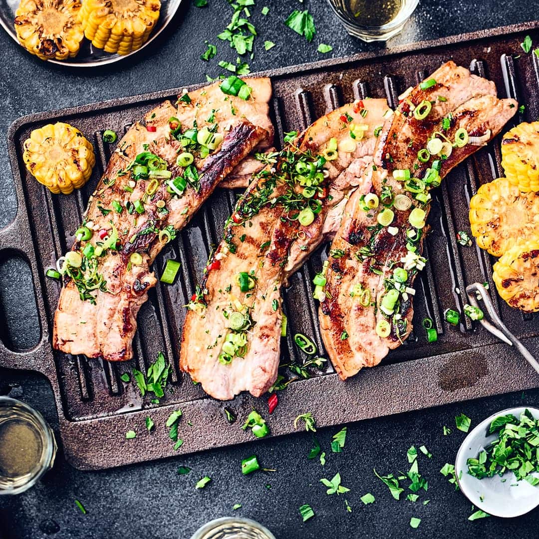 Pikant marinierte, magere Schweinebauchscheiben mit gegrillten Maiskolben. Perfekt für einen Grillabend geeignet.