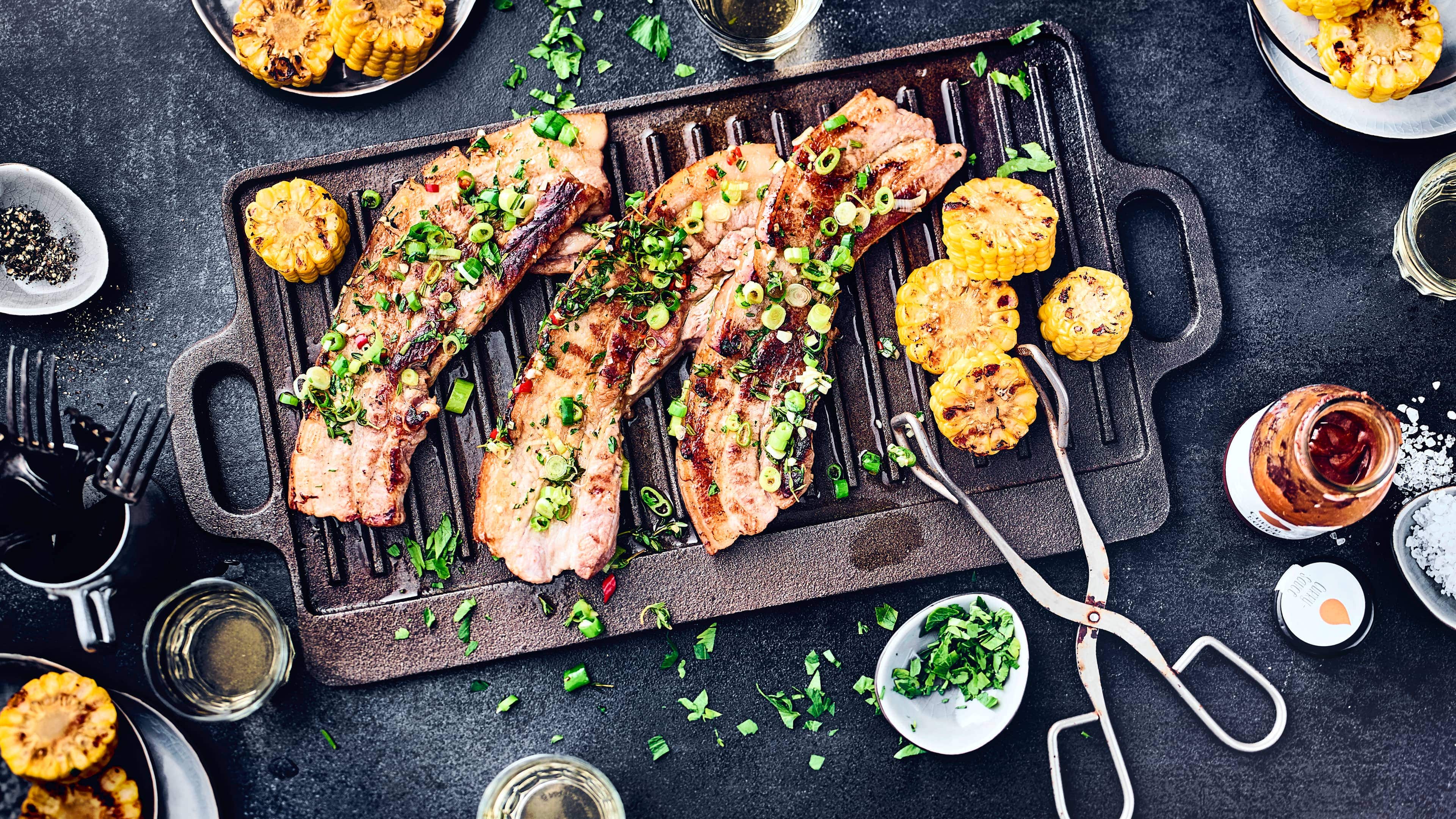 Gegrillter Schweinebauch Pikant marinierte, magere Schweinebauchscheiben mit gegrillten Maiskolben. Perfekt für einen Grillabend geeignet.