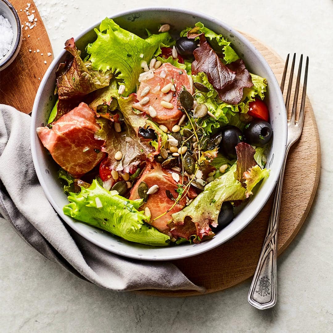Probieren Sie unser Rezept für knusprig gebratenen Ziegenfrischkäse einmal aus: umwickelt mit Serrano-Schinken an Lollo Rosso Salat mit Tomaten und Oliven!