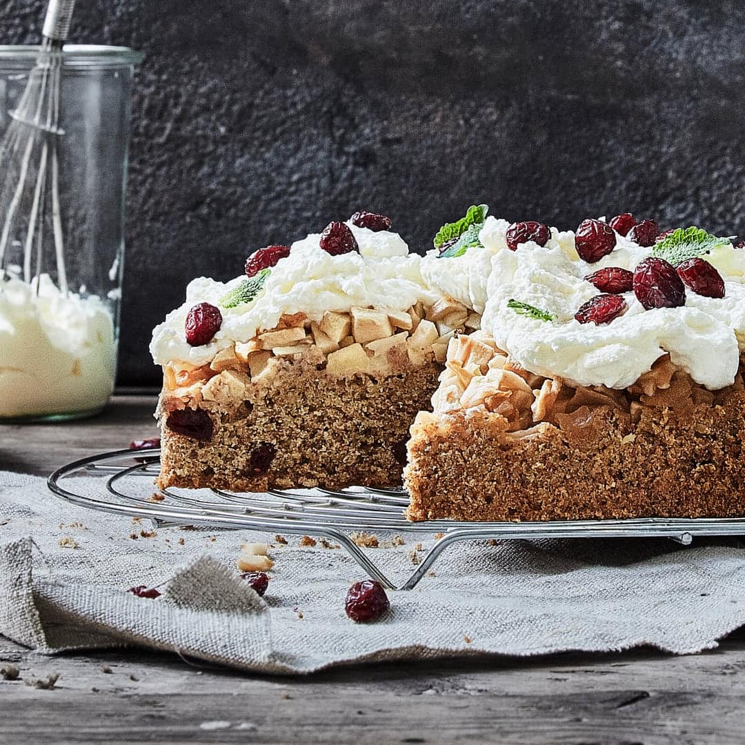 Fruchtiger Kuchen für Ihre Gäste: Probieren Sie unsere Apfeltorte mit Zimt, Mandeln und getrockneten Cranberries! Verziert wird mit Sahne und Beeren.