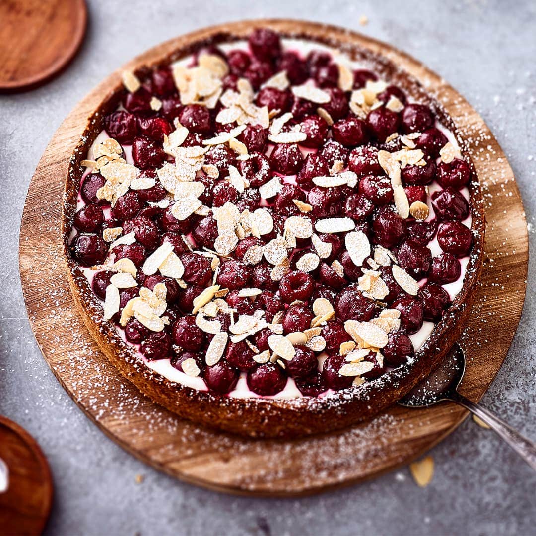 Köstlicher und erfrischender Kuchen mit einer Joghurtcreme bilden die ideale Unterlage für süße Kirschen und Mandelblättchen.