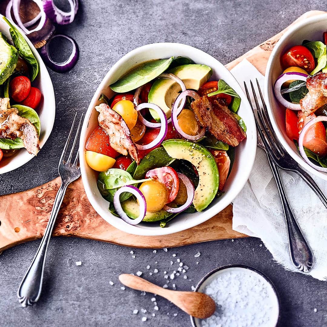 Allerlei leckere Zutaten und ein selbstgemachtes Apfel-Dressing ergeben unseren Tomaten-Avocado-Salat mit Tomaten, Avocado, gebratenem Speck und Babyspinat.