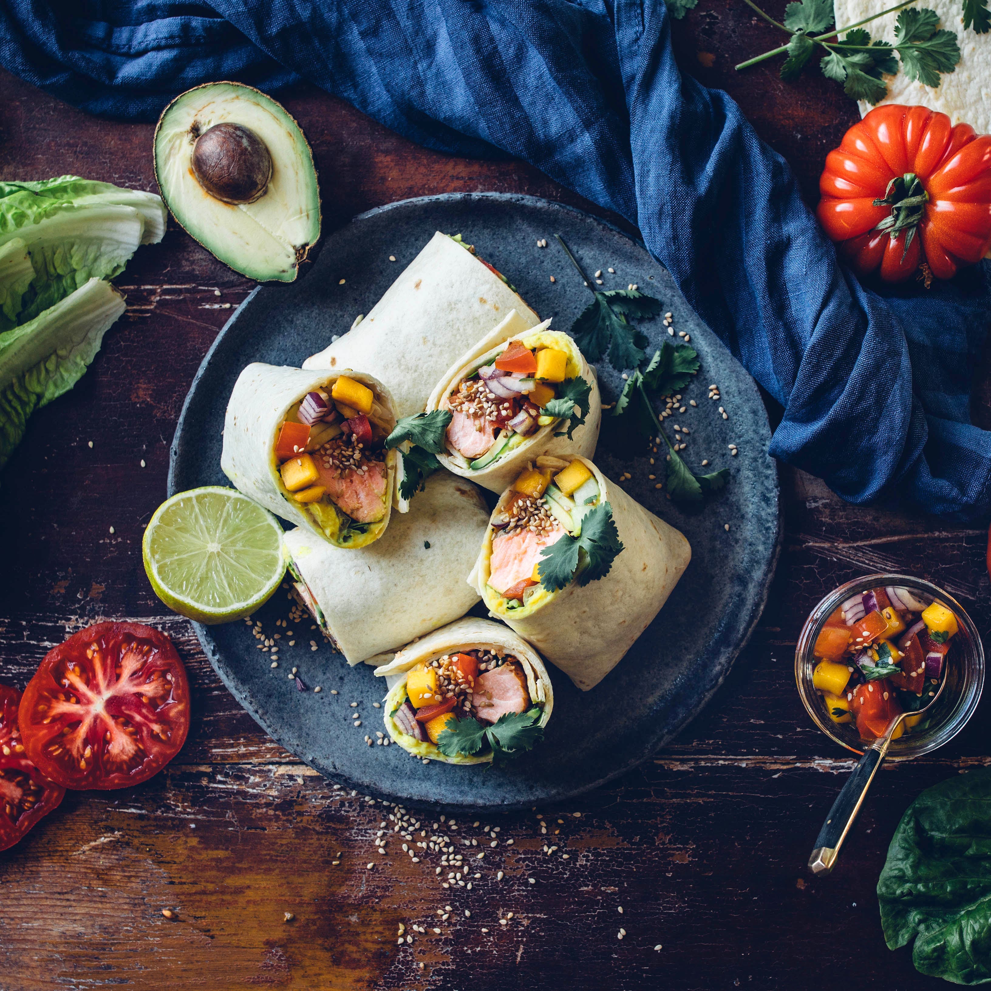 Wir servieren die leckeren Weizentortillas mit Lachs, Avocado und selbstgemachtem Bohnenmus. Eine würzige Mango-Salsa macht unsere selbstgemachten Lachs Wraps perfekt.
