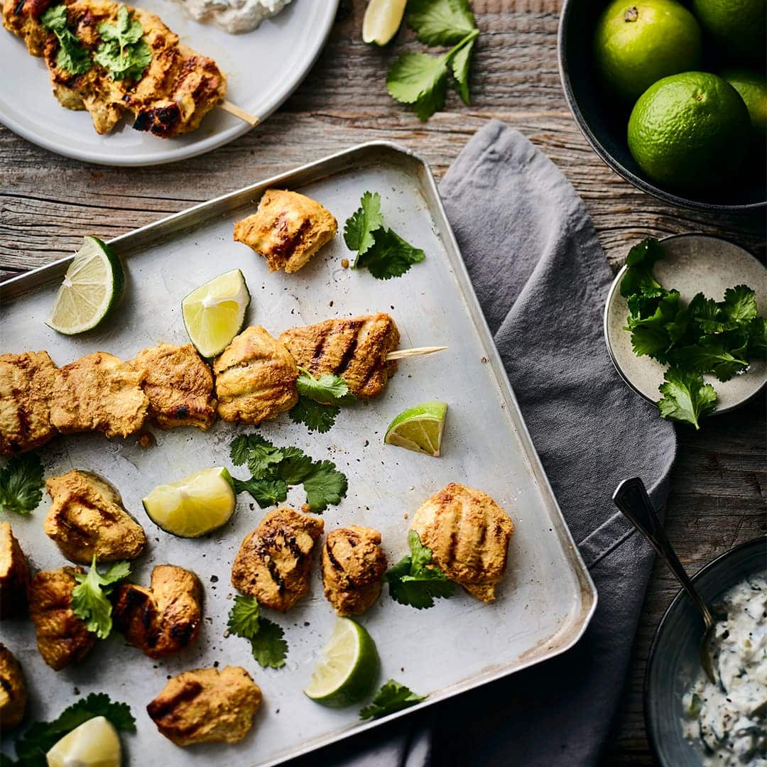 Allerlei Gewürze sowie frische Limetten geben den Hähnchenspießen vom Grill die köstliche Würze. Dazu passt Raita, ein indischer Joghurt-Dip.