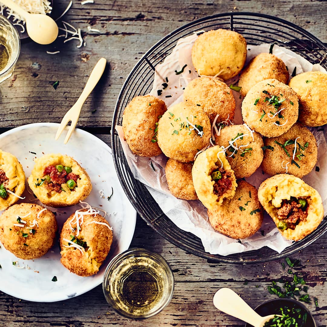 Arancini Bällchen sind köstliche kleine frittierte Reis-Bällchen, gefüllt mit Hackfleisch, Speck und Erbsen.