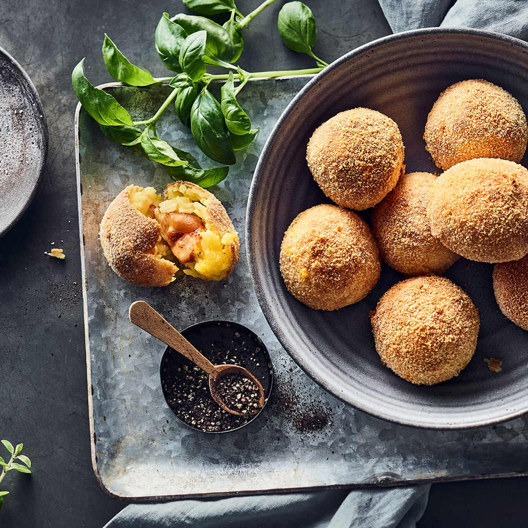 Knusprig frittierte Reisbällchen mit Käsefüllung, in einer Keramikschale, auf einem Metallblech