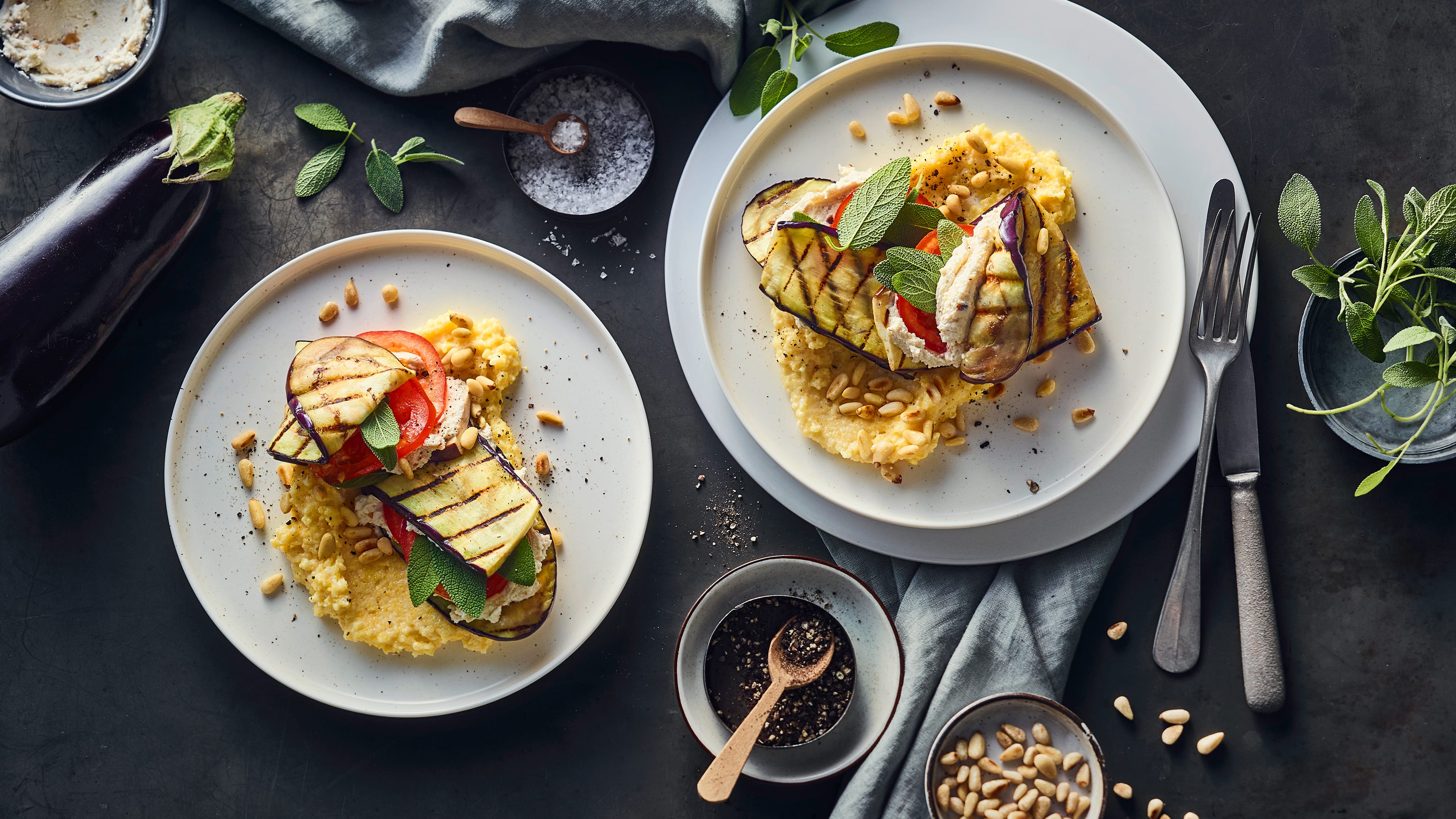 Gegrillte Auberginenscheiben mit Ricottacreme und Tomatenscheiben auf einem Bett aus Polenta, garniert mit Pinienkernen