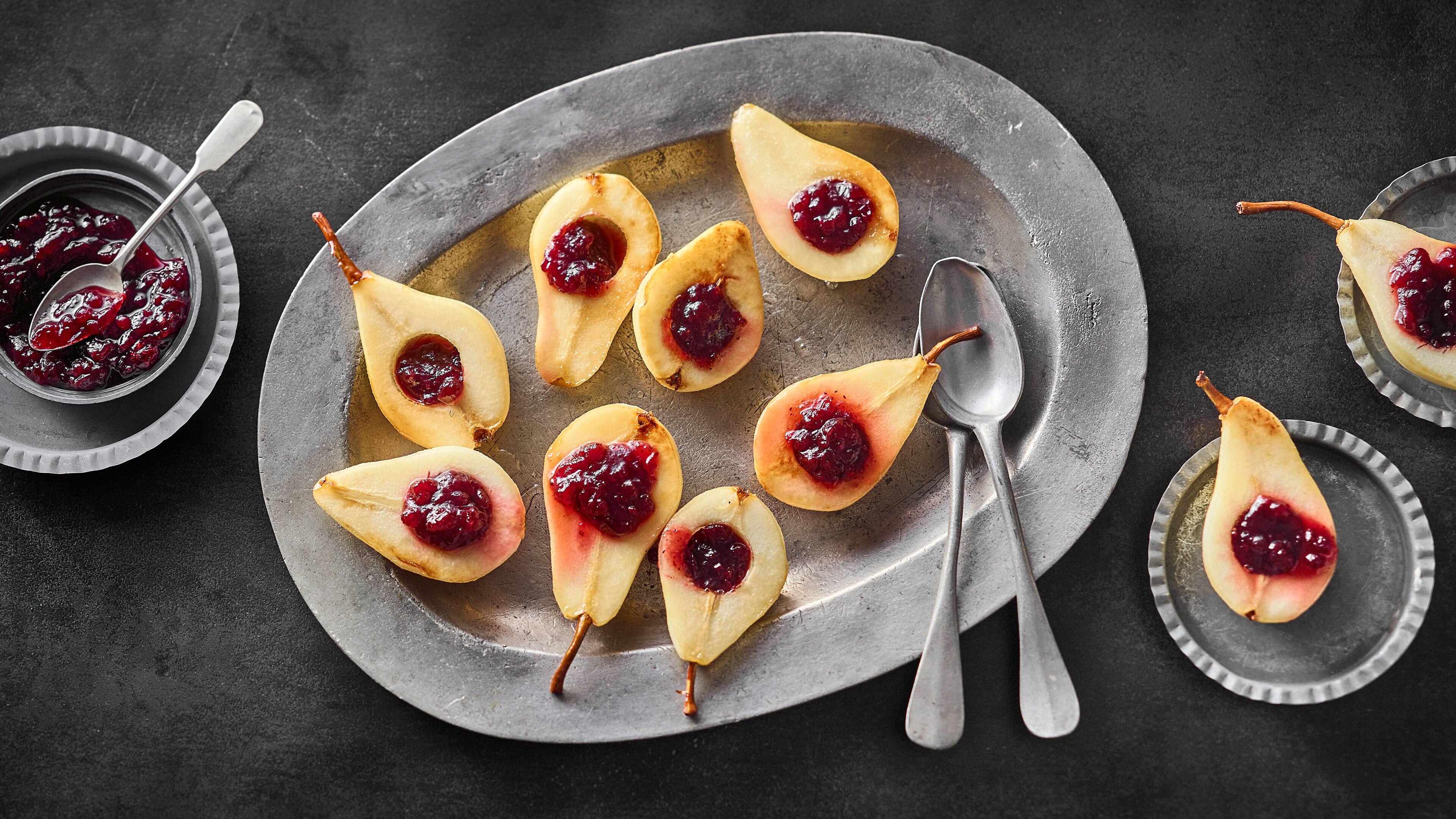 Rezept für karamellisierte Birnen mit Preiselbeeren Karamellisierte Birnenhälfen, getoppt mit Preiselbeeren, auf einer ovalen, rustikalen Schale